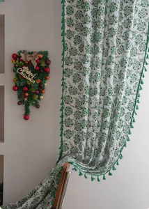 Detail of white kitchen curtain with green holly leaves and elegant green fringe tassels