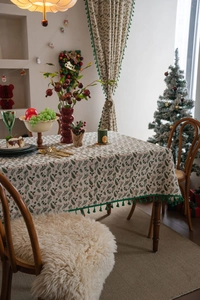 Detail of Christmas tablecloth featuring green holly leaf berry prints and tassel trim edges