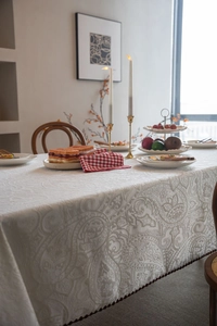Detail of cream-colored tablecloth featuring damascus jacquard patterns and brown tassels