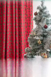 Detail of red Christmas curtain featuring gold tree patterns and soft plush ball trim