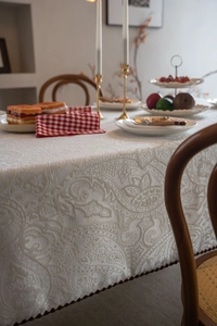 Close-up of ivory jacquard tablecloth with paisley patterns and dark red pompom trim details