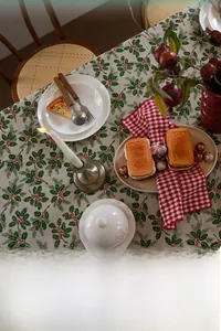 Close-up of festive holly leaf and red berry print on cream Christmas tablecloth