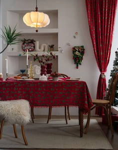 Detail der roten Weihnachtstischdecke mit grünen Bäumen und Plüschkugel-Fransenrand