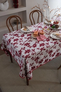 Dettaglio del motivo jacquard a foglie rosse su tovaglia bianco crema con bordo a onde rosso