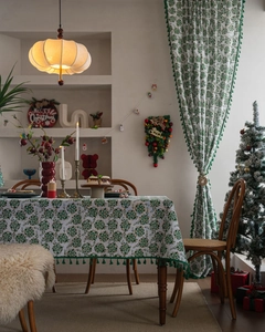 Detail view of festive tablecloth and curtains with green tassels and floral Christmas print
