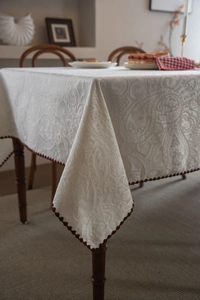 Detail of cream paisley jacquard tablecloth with elegant dark brown pompom edge trim