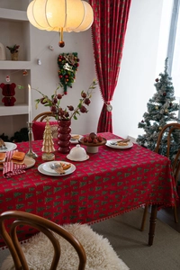 Detail der roten Weihnachtstischdecke mit grünen Tannenmustern und Bommelfransen am Rand