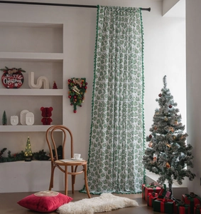 Detailed view of white Christmas curtains with green holly leaf prints and fringe trim