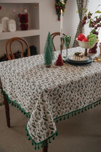 Detailed view of Christmas tablecloth with holly berry patterns and green fringe tassels