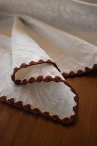 Detailed close-up of French luxury white jacquard tablecloth with brown scalloped crochet edges
