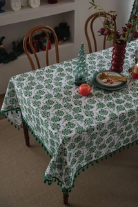 Close-up of a white Christmas tablecloth with green floral prints and tassel edges