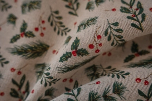 Macro shot of Christmas holly leaves and red berries on a textured linen festive tablecloth