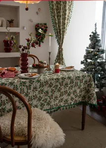 Detail of Christmas tablecloth featuring holly leaf berry print and green tassel fringe edge