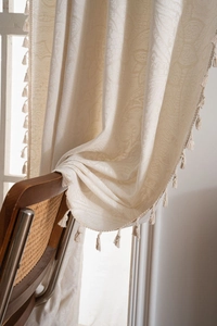 Detail of cream jacquard curtain with damask pattern and elegant tassel trim on vintage chair