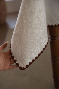 Macro detail of cream jacquard tablecloth fabric with brown scalloped trim and damask pattern