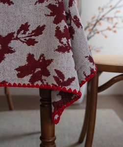 Dettaglio macro della tovaglia jacquard grigia con motivi a foglia rossa e bordi a onde