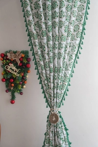 Close-up of Christmas curtain with green snowflake print, tassels and reindeer charm
