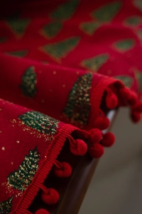 Detail eines roten Weihnachts-Tischläufers mit grünen Bäumen und weichen Bommeln
