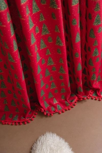 Detail of red Christmas fabric with green tree patterns and decorative pompom fringe