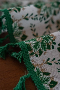 Detail of Christmas tablecloth with green holly leaves, golden berries and woven tassels