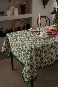 Close-up of Christmas tablecloth with holly leaf prints and dark green tassel edges