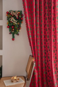 Close-up of red Christmas curtain with green tree patterns and decorative red pompoms