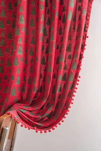 Close-up of red Christmas curtain with golden tree print and decorative pom-pom edges