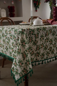 Detailed close-up of Christmas holly leaf print tablecloth with green tassel edge