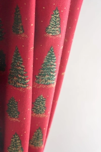 Detailed close-up of red Christmas curtain with shimmering gold foil green tree patterns