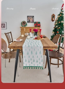 Close-up of beige linen Christmas table runner with green tree prints and tassels