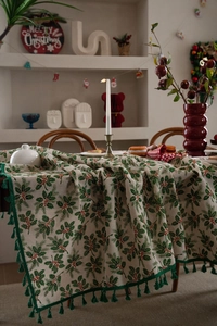 Detail of Christmas tablecloth featuring green holly leaves, red berries, and green tassels