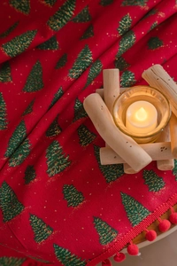 Detail of red Christmas curtain with green tree prints and pom-pom trim in a cozy setting