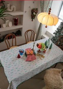 Close-up of green pine tree print and ball fringe tassel edge on white Christmas tablecloth