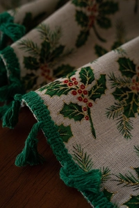 Close-up of Christmas table runner with holly leaves, red berries, and green tassels