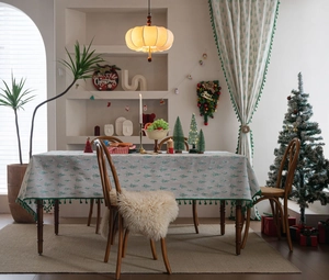 Detail view of Christmas tablecloth featuring green pine tree prints and tassel fringe edges