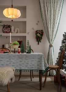 Close-up of beige Christmas tablecloth with green tree prints and emerald tassel edges