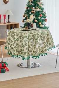 Detail of Christmas round tablecloth with holly print and dark green fringe edges