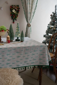 Detail of Christmas tablecloth with green pine tree prints and festive tassel fringe