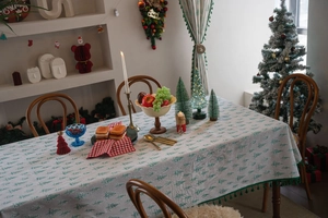 Detail of Christmas tablecloth featuring green pine tree prints and decorative pom-poms fringe