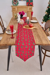Detail of red Christmas table runner with green gold tree patterns on a wooden table