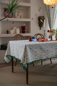 Detailed view of green Christmas tree patterns and fringe tassels on a cream tablecloth