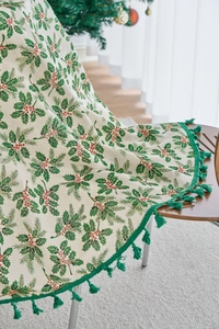Detail of pine branch print tablecloth with green tassels and holly berry pattern