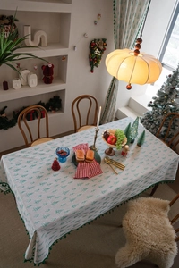 Close-up of Christmas tablecloth featuring green pine tree prints and ball tassel edges