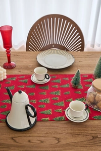 Detail view of red Christmas table runner with green tree prints on wooden dining table