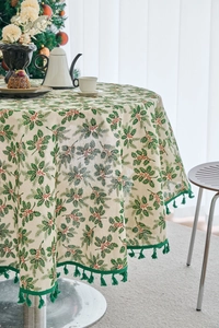 Detail of Christmas round tablecloth with holly leaf print and green tassel fringe