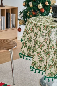 Detail of round Christmas tablecloth with holly berry print and green tassel fringe