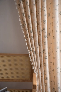 Detailed close-up of cream curtain fabric with floral print and white tassel trim