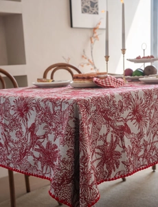 Detailed texture of Toile de Jouy tablecloth with red pom-pom fringe and floral patterns