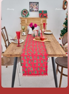 Close-up of red Christmas table runner with green tree prints and red pompom fringe trim