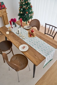 Close-up of a Christmas table runner with green pine tree prints and dark green tassels